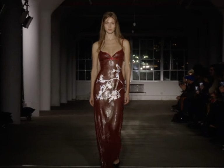 Model walking down the runway in a sheer, burgundy sparkly dress with floral detailing at the Ludovic de Saint Sernin NYFW show 2024. 
